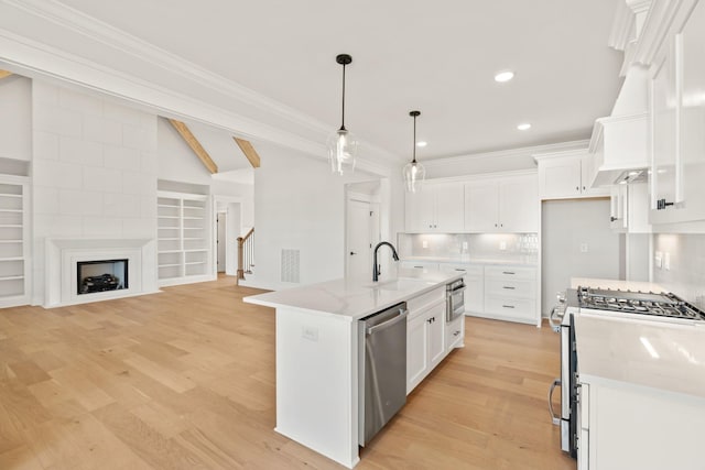 kitchen with light stone counters, a center island with sink, appliances with stainless steel finishes, white cabinets, and a sink