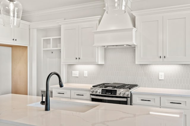 kitchen featuring stainless steel gas range oven, custom range hood, light stone counters, white cabinetry, and a sink