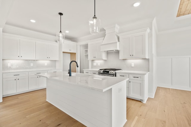 kitchen featuring a kitchen island with sink, a sink, white cabinetry, stainless steel range with gas stovetop, and custom range hood