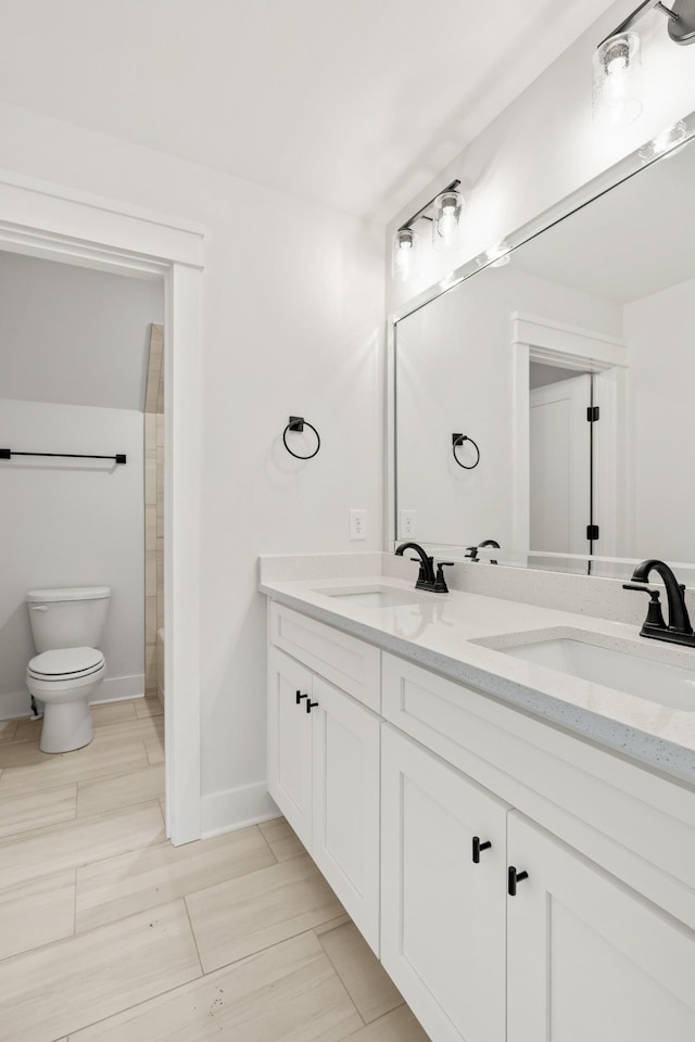 full bath featuring baseboards, a sink, toilet, and double vanity