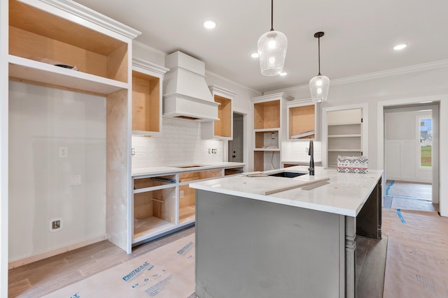 kitchen featuring pendant lighting, sink, premium range hood, a kitchen island with sink, and crown molding