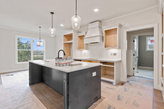 kitchen featuring premium range hood, black electric stovetop, ornamental molding, pendant lighting, and an island with sink