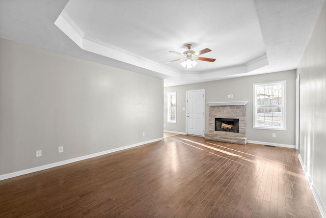 unfurnished living room with hardwood / wood-style floors, a stone fireplace, a raised ceiling, and ceiling fan