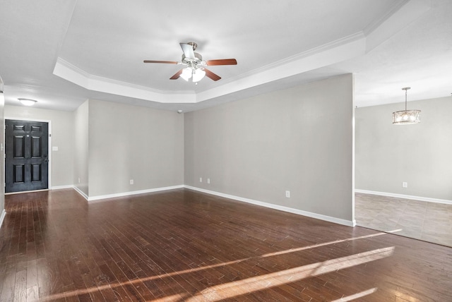 empty room featuring crown molding, ceiling fan with notable chandelier, dark hardwood / wood-style flooring, and a tray ceiling