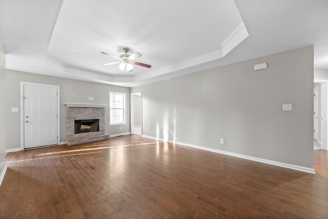 unfurnished living room with a raised ceiling, a stone fireplace, dark wood-type flooring, and ceiling fan