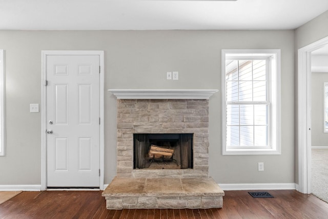 unfurnished living room featuring dark hardwood / wood-style floors, a healthy amount of sunlight, and a stone fireplace