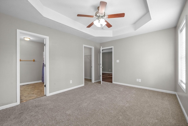 unfurnished bedroom featuring carpet, a spacious closet, ceiling fan, a tray ceiling, and a closet