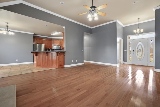 unfurnished living room featuring light wood-type flooring, ceiling fan with notable chandelier, crown molding, and sink