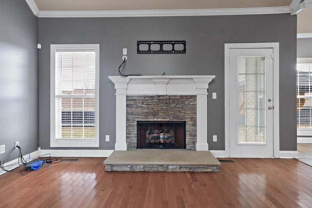 unfurnished living room with crown molding, plenty of natural light, a stone fireplace, and wood-type flooring