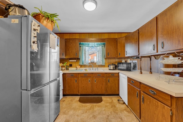 kitchen with sink, dishwasher, stainless steel refrigerator, and wooden walls