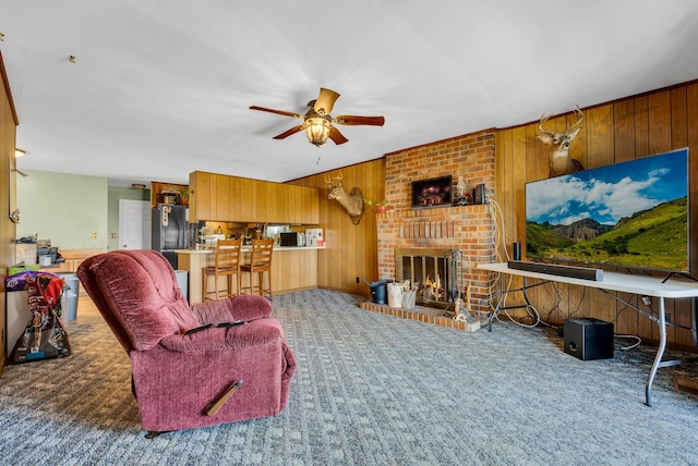 carpeted living room featuring ceiling fan, wooden walls, and a fireplace