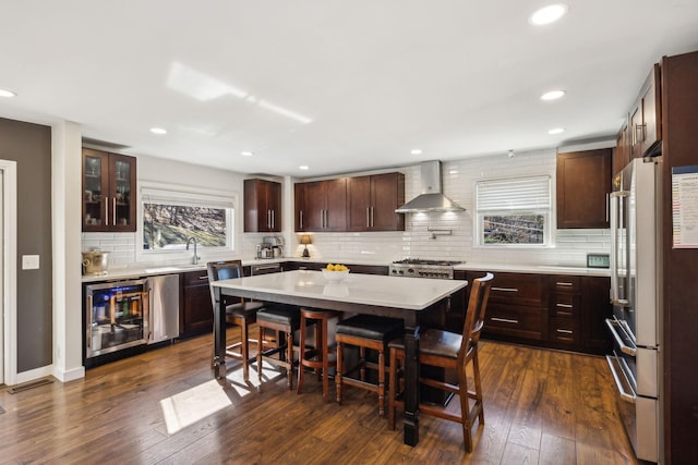 kitchen with high end refrigerator, a kitchen breakfast bar, dark hardwood / wood-style flooring, a center island, and wall chimney exhaust hood