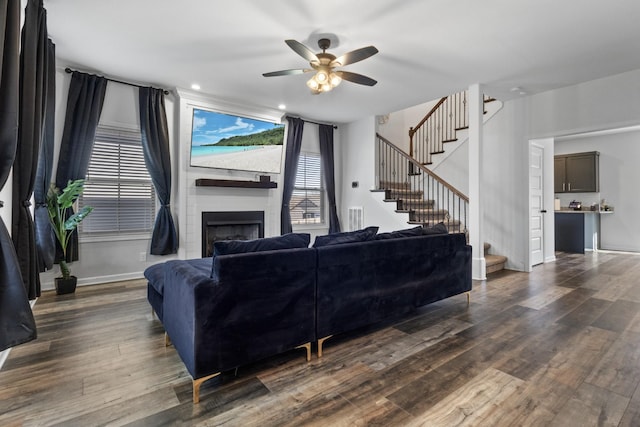 living room featuring ceiling fan, a large fireplace, and dark hardwood / wood-style floors