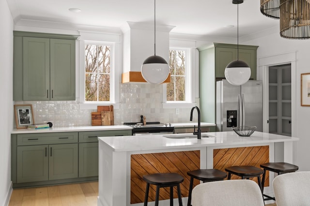 kitchen featuring an island with sink, sink, hanging light fixtures, stainless steel fridge with ice dispenser, and green cabinetry