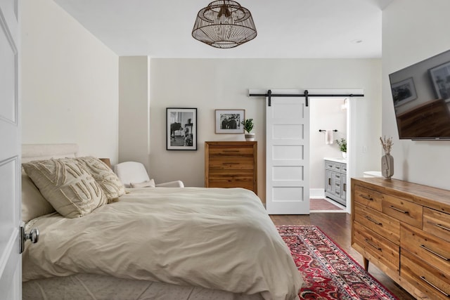 bedroom featuring dark hardwood / wood-style floors, ensuite bath, and a barn door