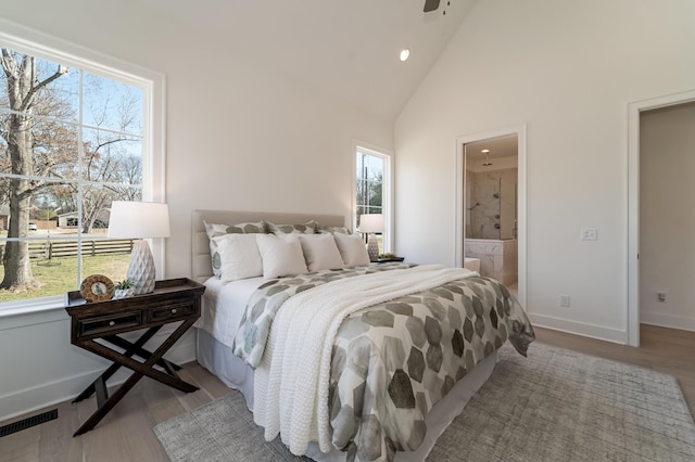 bedroom featuring light wood-type flooring, high vaulted ceiling, connected bathroom, and multiple windows