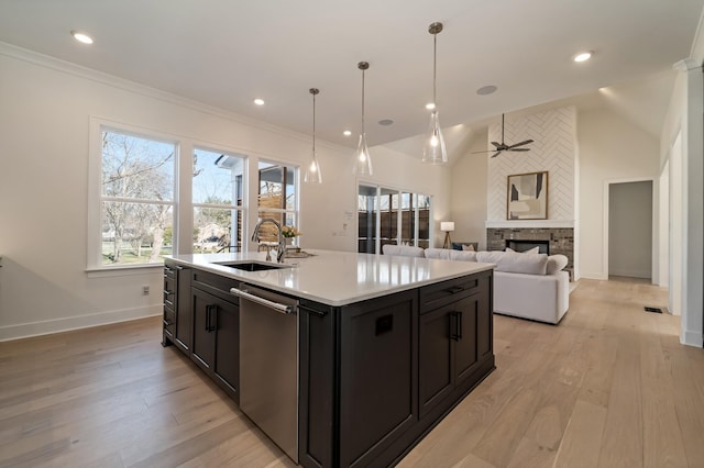 kitchen with dishwasher, sink, decorative light fixtures, a stone fireplace, and a kitchen island with sink