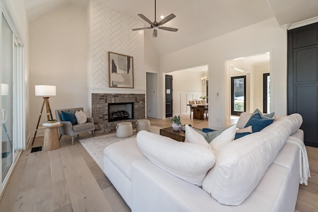 living room with lofted ceiling, light wood-type flooring, ceiling fan, and a brick fireplace