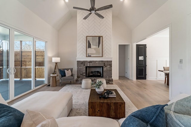 living room featuring a brick fireplace, lofted ceiling, ceiling fan, and light wood-type flooring