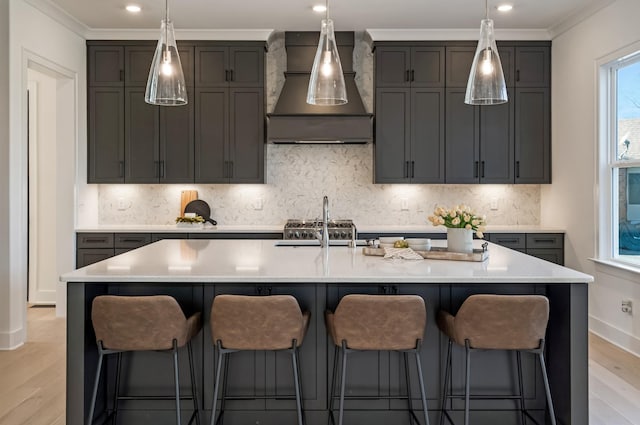 kitchen featuring plenty of natural light, a kitchen island with sink, light hardwood / wood-style flooring, and wall chimney range hood