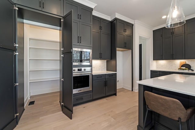 kitchen with light wood-type flooring, stainless steel appliances, ornamental molding, and pendant lighting