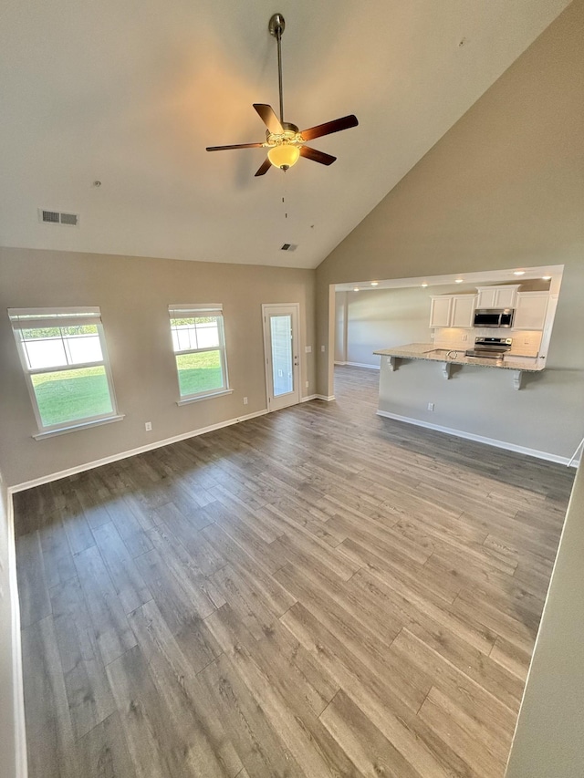 unfurnished living room featuring light hardwood / wood-style floors, high vaulted ceiling, and ceiling fan