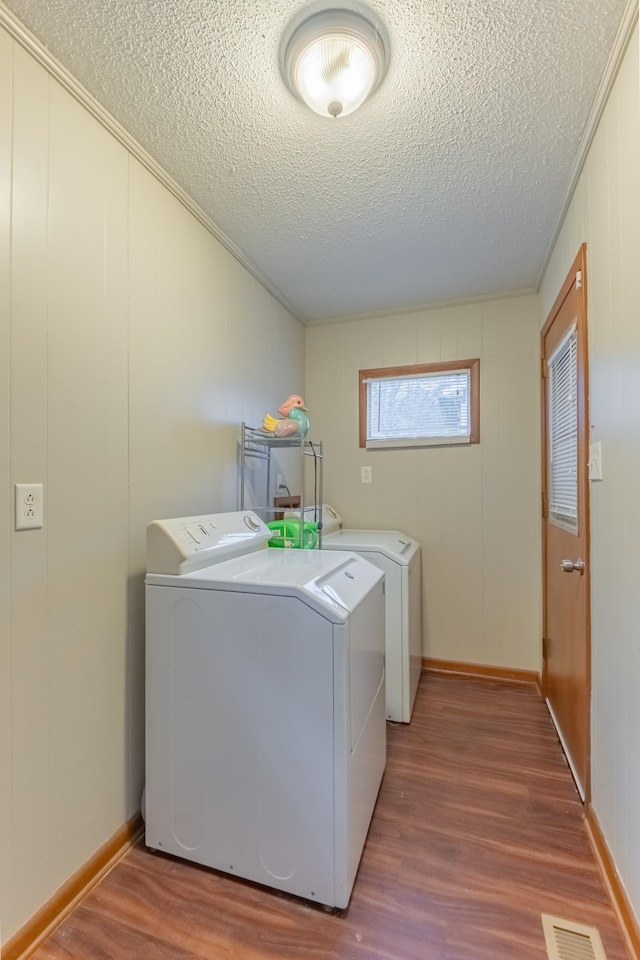 clothes washing area featuring wood-type flooring, wood walls, separate washer and dryer, and ornamental molding