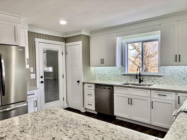 kitchen featuring appliances with stainless steel finishes, light stone countertops, backsplash, sink, and white cabinetry