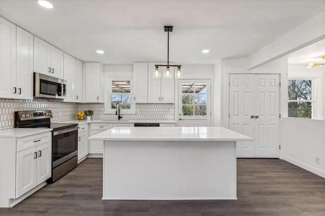 kitchen featuring white cabinets, appliances with stainless steel finishes, a center island, sink, and hanging light fixtures