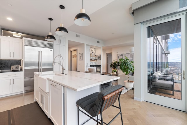 kitchen with built in refrigerator, light stone countertops, hanging light fixtures, and white cabinets