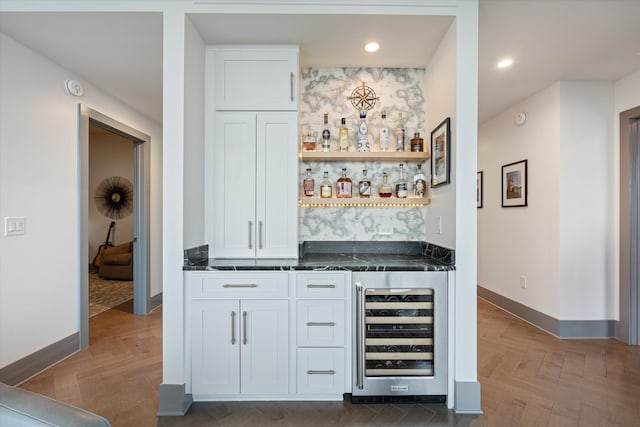 bar with dark parquet floors, white cabinetry, dark stone counters, and wine cooler