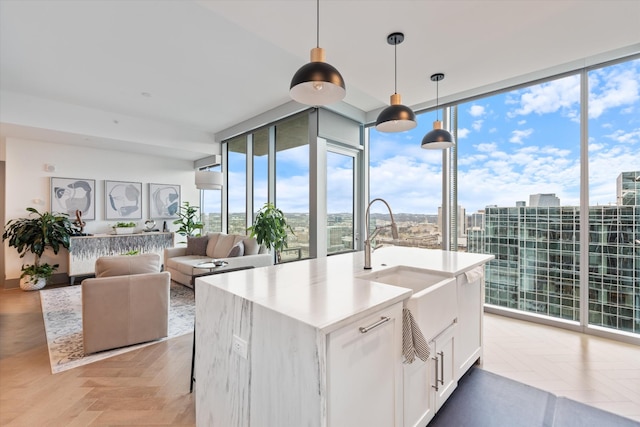 kitchen featuring pendant lighting, white cabinets, plenty of natural light, expansive windows, and a center island with sink