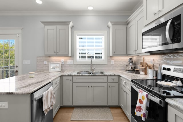 kitchen featuring kitchen peninsula, appliances with stainless steel finishes, sink, light stone counters, and decorative backsplash