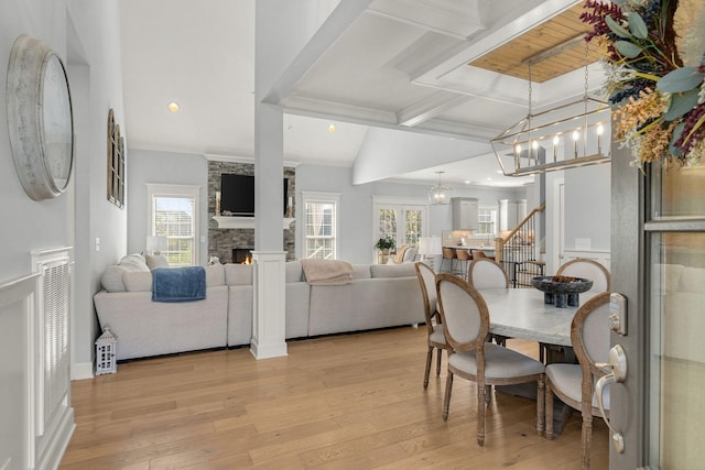 dining room with light wood-type flooring, a stone fireplace, a healthy amount of sunlight, and beam ceiling