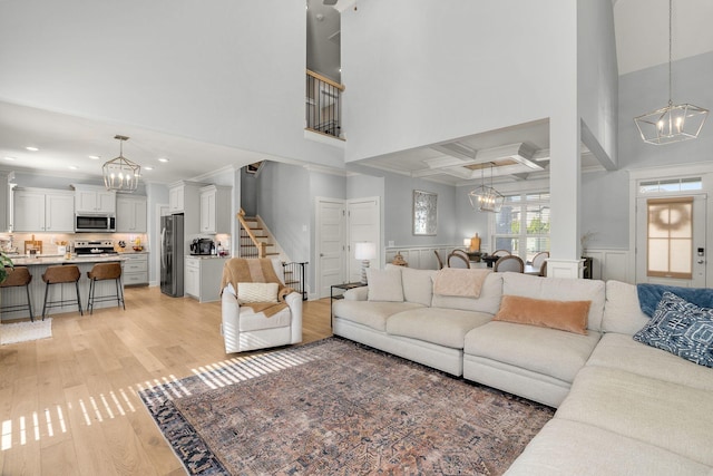 living room featuring light wood-type flooring, coffered ceiling, a chandelier, and beam ceiling