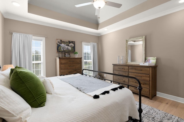 bedroom featuring ceiling fan, a raised ceiling, light hardwood / wood-style flooring, and multiple windows