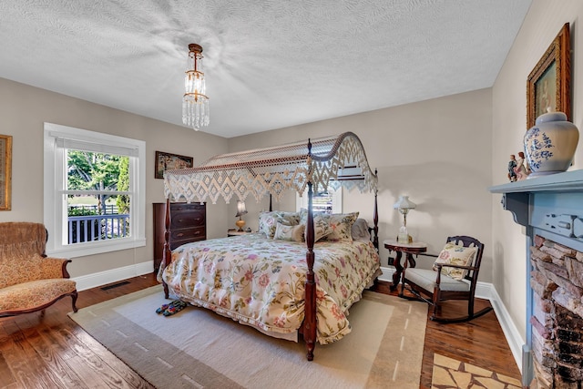 bedroom with hardwood / wood-style flooring, a textured ceiling, and a stone fireplace