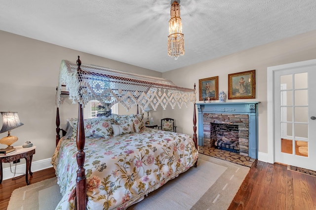 bedroom with an inviting chandelier, a textured ceiling, a fireplace, and wood-type flooring