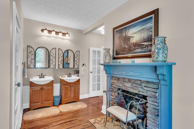 bathroom with hardwood / wood-style flooring, a textured ceiling, vanity, and a stone fireplace