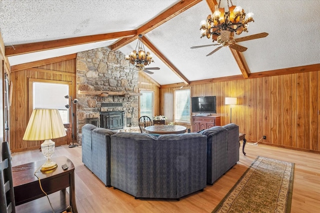 living room featuring ceiling fan with notable chandelier, a textured ceiling, a stone fireplace, vaulted ceiling with beams, and light hardwood / wood-style floors