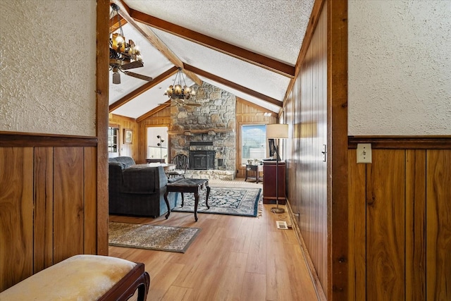 living room featuring ceiling fan, hardwood / wood-style flooring, lofted ceiling with beams, a fireplace, and a textured ceiling