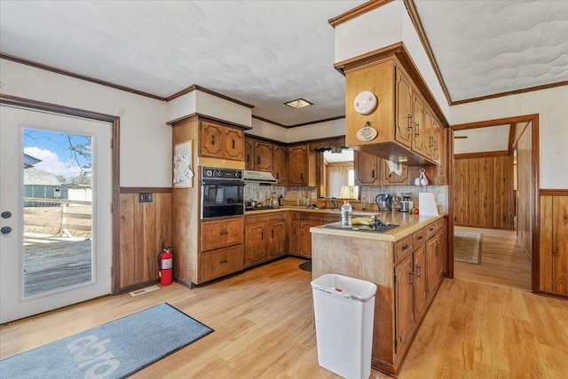 kitchen with black appliances, tasteful backsplash, sink, light wood-type flooring, and crown molding