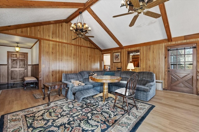 living room featuring ceiling fan with notable chandelier, wooden walls, lofted ceiling with beams, and light wood-type flooring