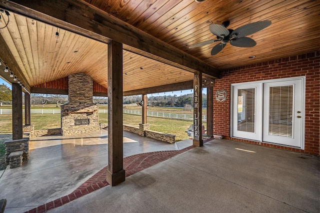 view of patio with ceiling fan, an outdoor stone fireplace, and a rural view