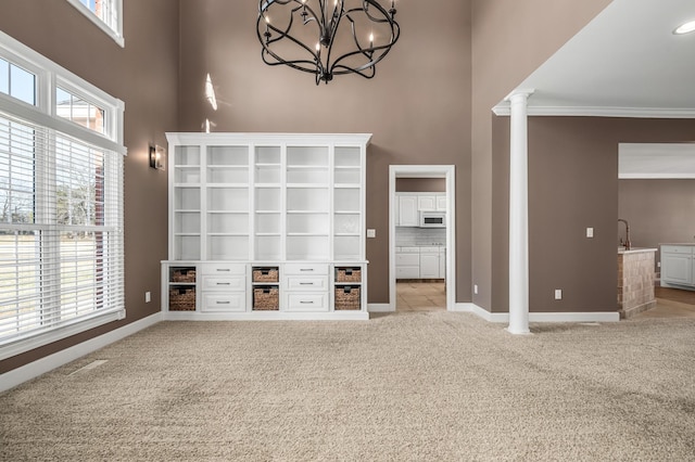 unfurnished living room with light carpet, decorative columns, a notable chandelier, and plenty of natural light