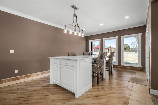 kitchen featuring a kitchen island, white cabinetry, hanging light fixtures, ornamental molding, and a breakfast bar area