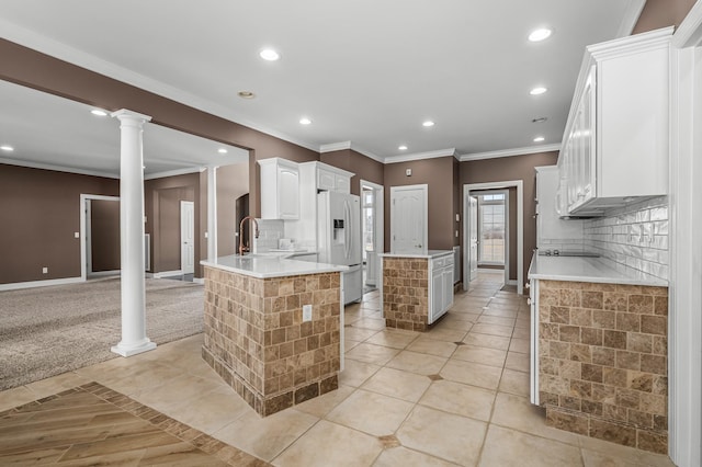 kitchen featuring ornate columns, white fridge with ice dispenser, white cabinetry, decorative backsplash, and a kitchen island