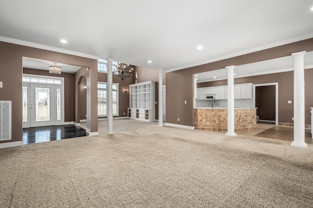 unfurnished living room with ornamental molding, a chandelier, carpet flooring, and ornate columns