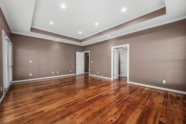 empty room with a tray ceiling, dark hardwood / wood-style floors, and crown molding