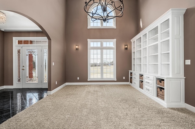 entryway featuring dark colored carpet, a chandelier, and a towering ceiling